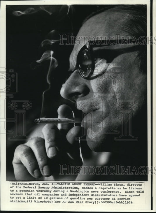 1974 Press Photo William Simon smokes a cigarette as he listens to a question - Historic Images