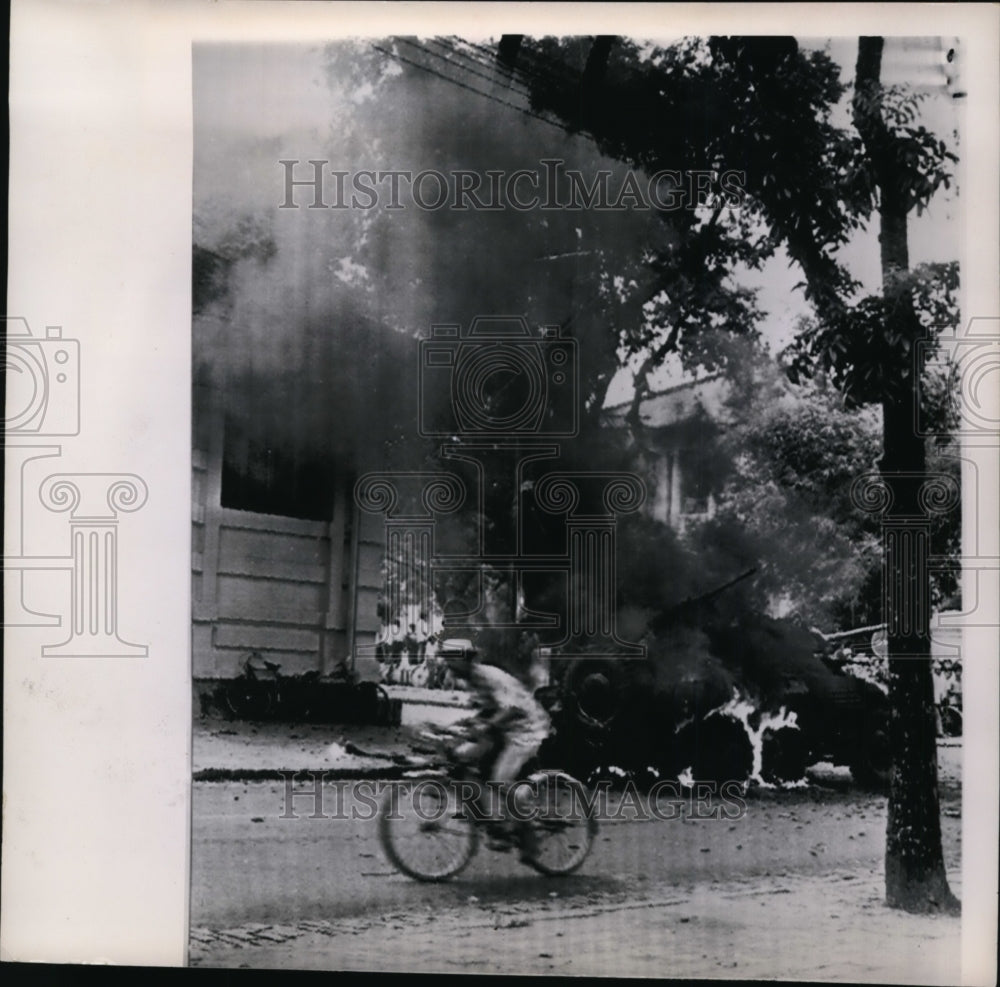 1960 Press Photo A cyclist rides past a burning armored car in Saigon street - Historic Images