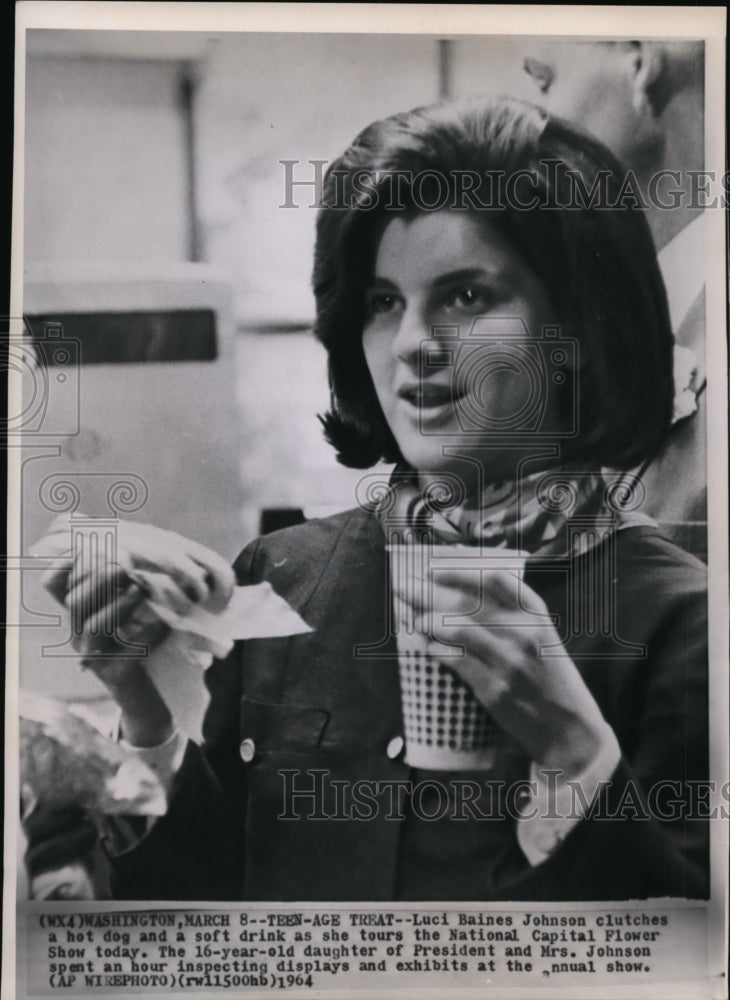 1964 Press Photo Luci Baines Johnson clutches a hot dog and a soft drink as she - Historic Images