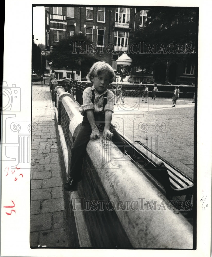 1983 Child rests astride a fence in park - Historic Images