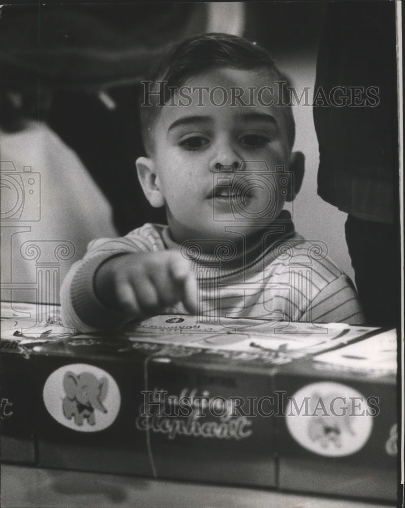 1964 Press Photo Child Tommy Mitchmore Looks at Package With Elephant Logo. - Historic Images