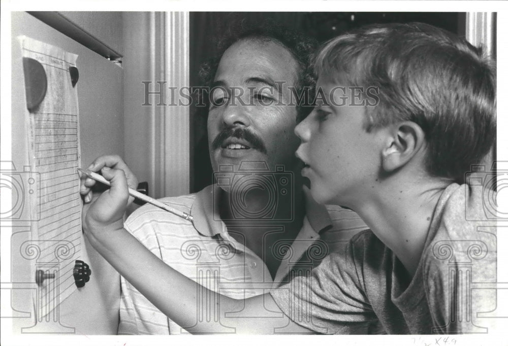 1982 Tom Foster and son Clay review chore chart in Houston, TX - Historic Images