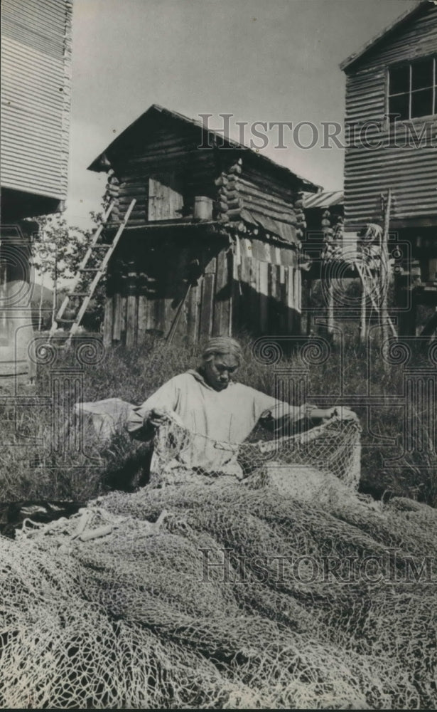 1974 Mrs. Faith Moyer mends a fishing net in front of Eskimo homes - Historic Images