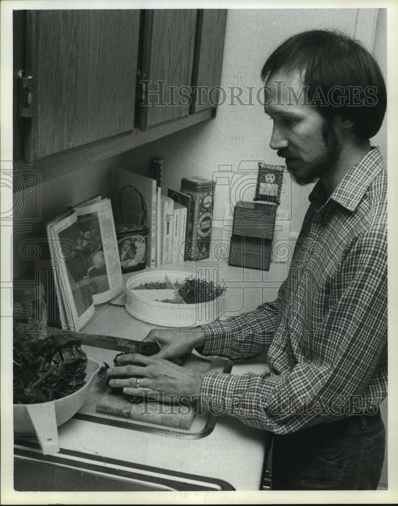 1983 Man chops vegetables and follows cookbook - Historic Images