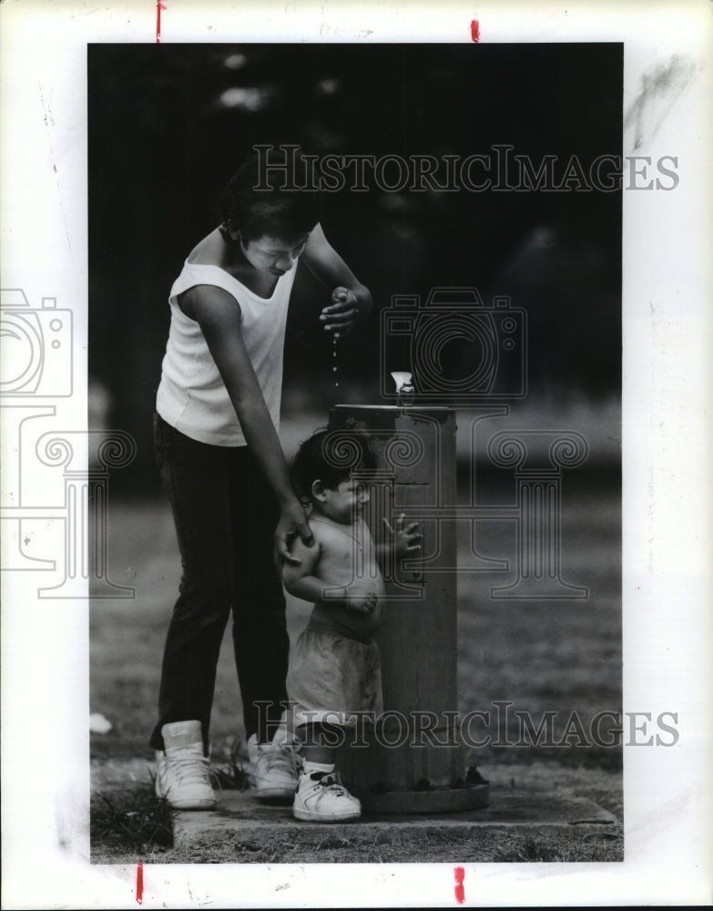 1990 Jose Mendes pours water on Rene Flores in Hermann Park, Houston - Historic Images