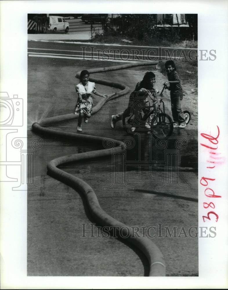 1991 Children play in water spray created by Houston firemen hose - Historic Images