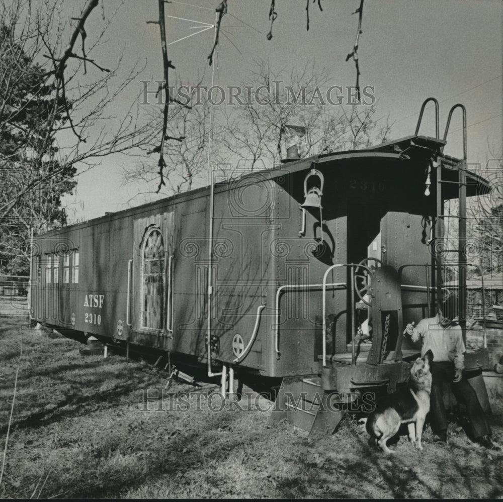 1977 Press Photo Man with dog leans on back of old freight car off tracks - Historic Images