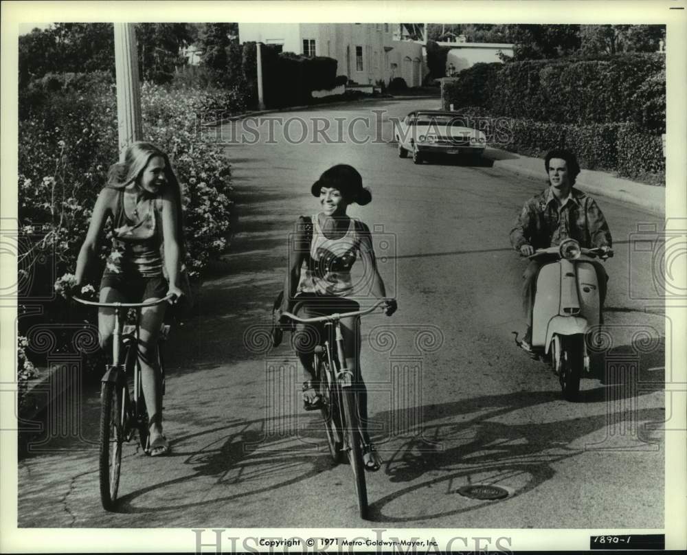 1971 Scene with two women on bikes and man on motorbike. - Historic Images