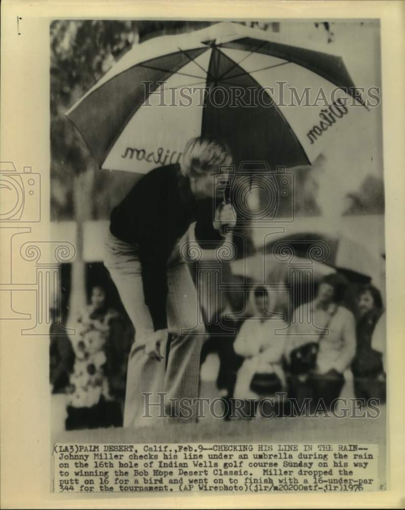 1976 Press Photo Golfer Johnny Miller holds umbrella as he checks his line in CA- Historic Images