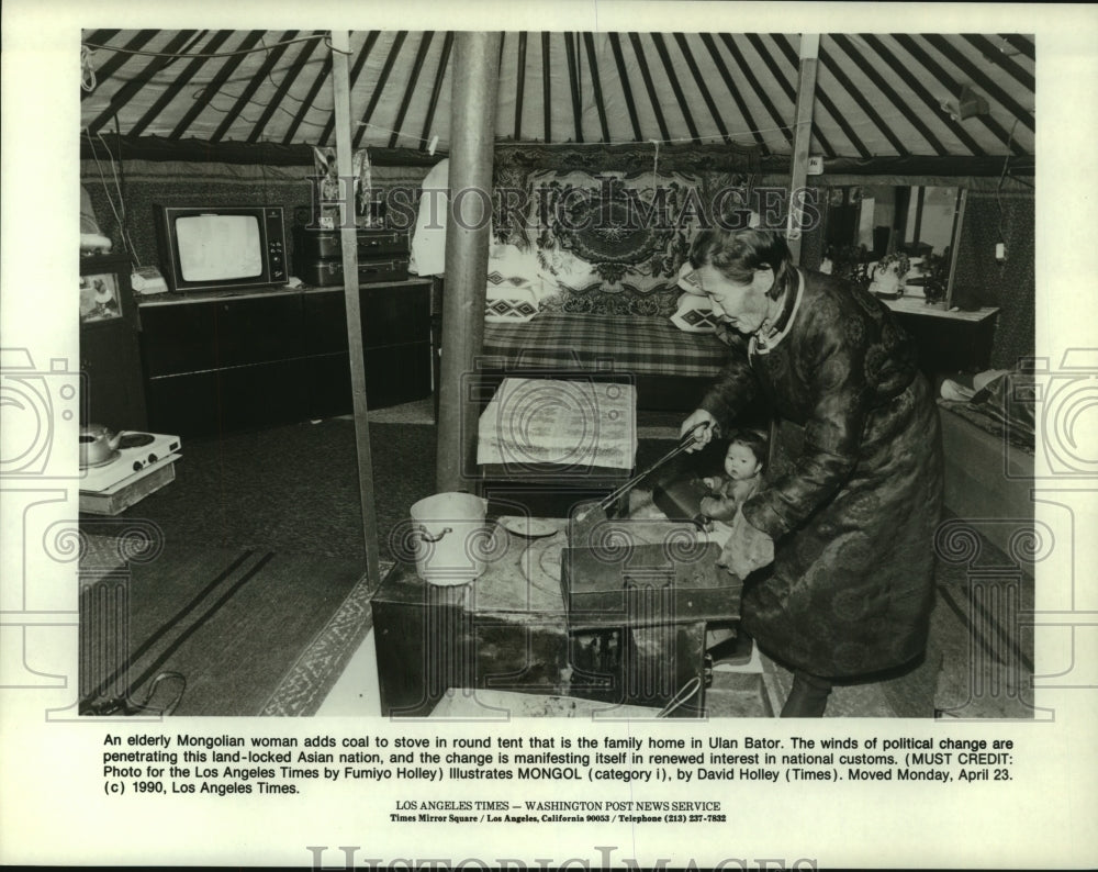 1990 Press Photo Elderly Mongolian Woman Adds Coal To Stove in Family Home.-Historic Images