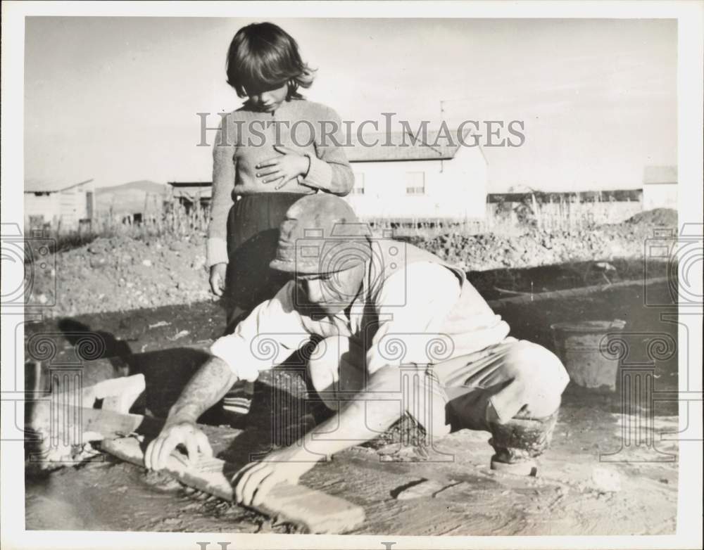 1964 Press Photo A man works on a house in Arad, Israel, as his daughter watches- Historic Images