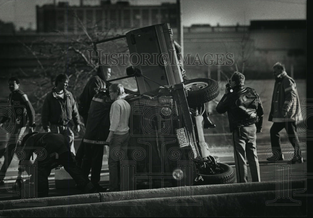 1990 Press Photo Rescuers examine overturned vehicle in East-West Freeway-Historic Images