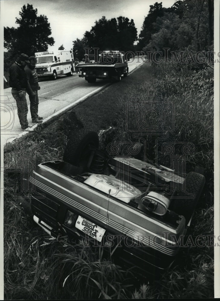 1991 Press Photo Tow truck operators examine a car that rolled over in the ditch - Historic Images