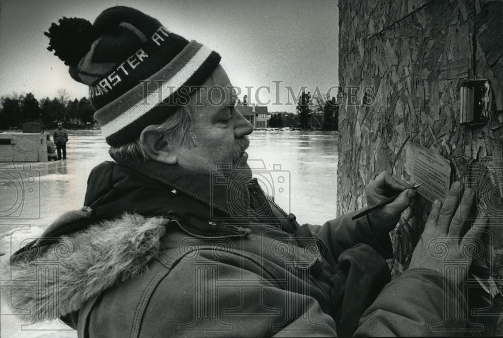 1989 Press Photo Lou Ottmer writes a warning on Big Cedar Lake Fishing Shed-Historic Images