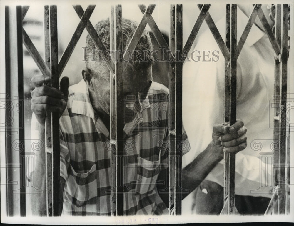 1963 Press Photo Man peers from behind the metal bars of a gate in Santo Domingo-Historic Images