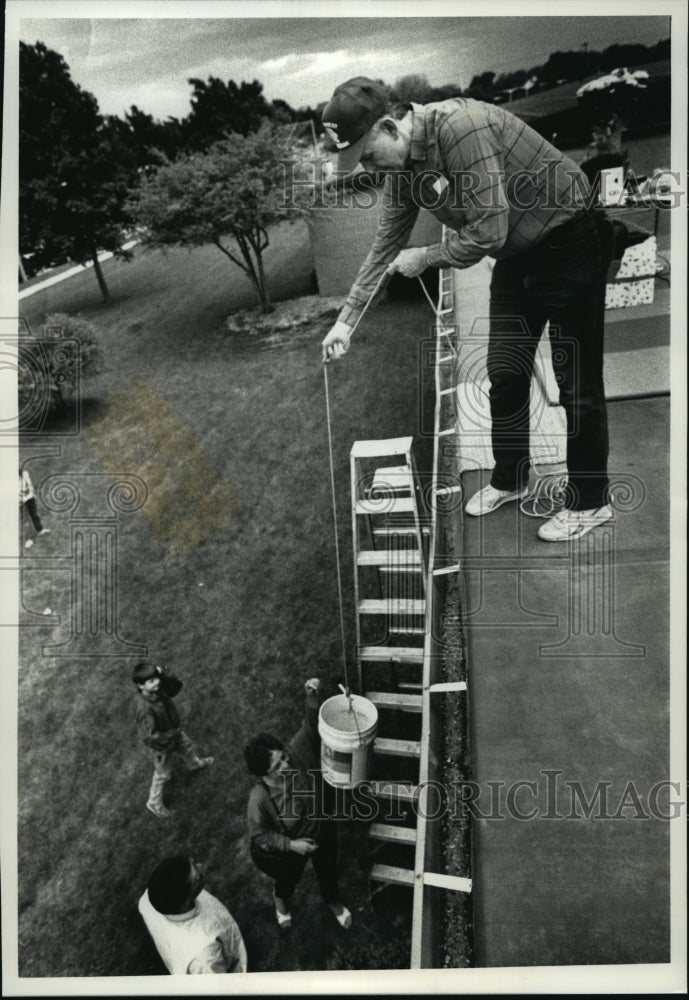 1990 Press Photo Roger Laesch, collects donations in a bucket from school roof - Historic Images