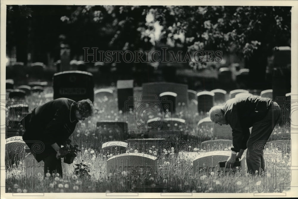 1986 Press Photo A couple planted flowers and clearing weeds around graves - Historic Images