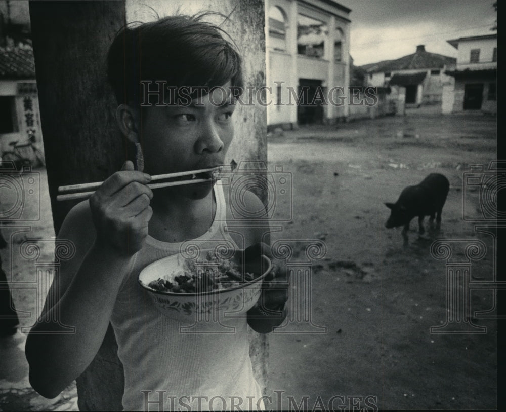 Press Photo Young man in farming village uses chopsticks to eat, China - Historic Images