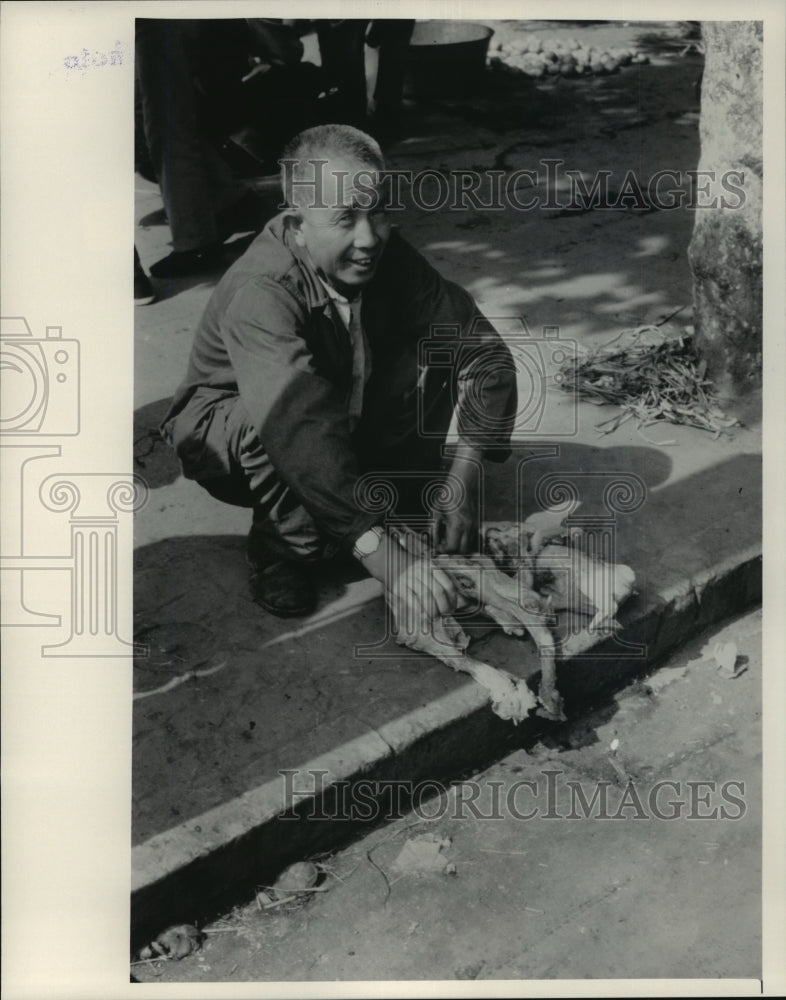 1982 Press Photo Chinese man cleaning chicken on sidewalk - mja82862 - Historic Images