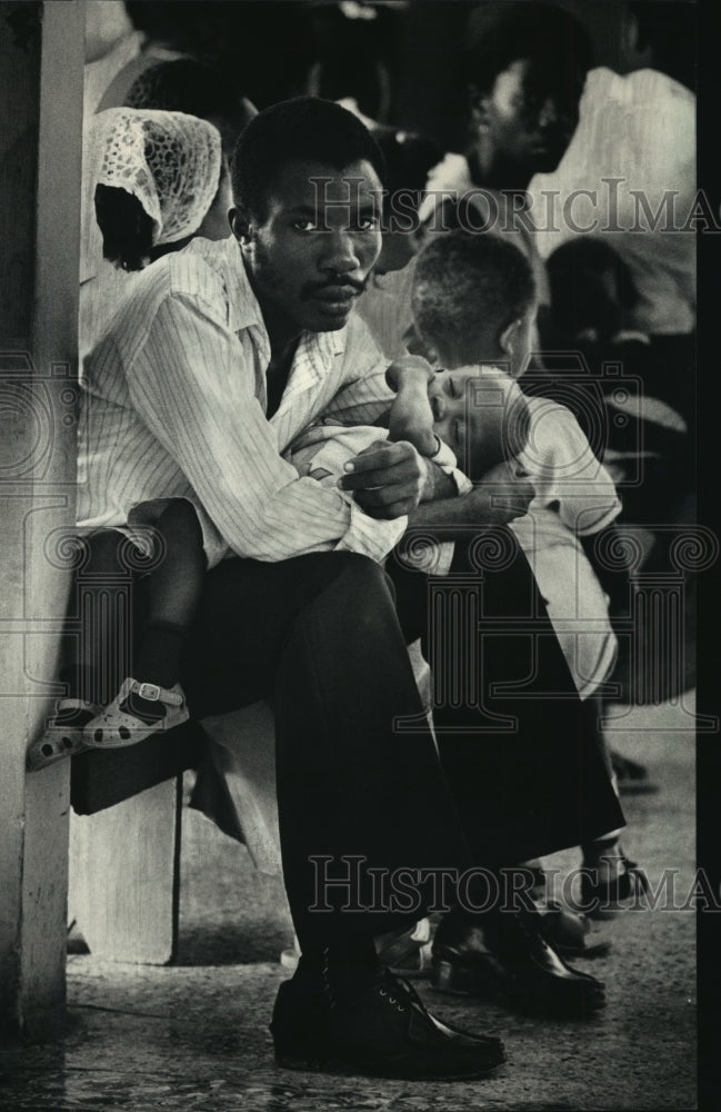 1987 Press Photo Raphael DeSalles holds his son, waiting to see a doctor - Historic Images