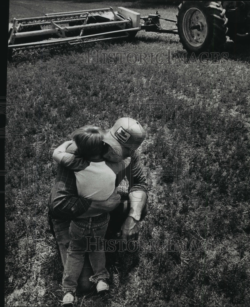 1988 Press Photo Ron Kutz hugs his son after cutting hay on farm near Jefferson.-Historic Images