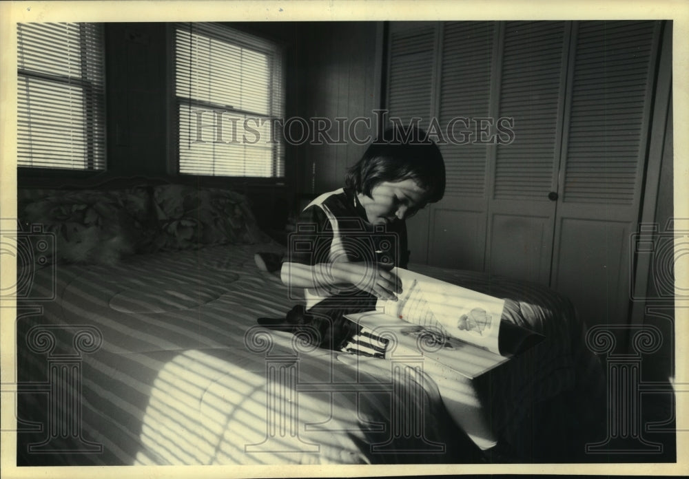 1993 Press Photo Ashley Nichole Dile seated on her bed looks at one of her books - Historic Images