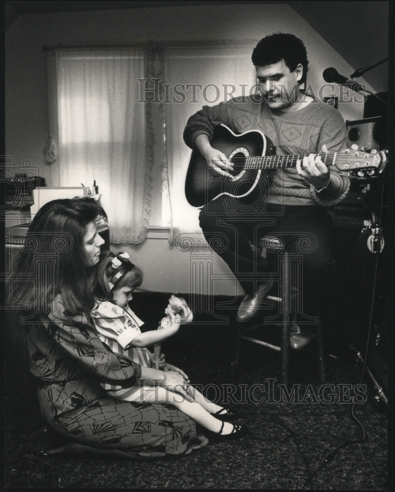 1989 Press Photo Mel Santiago plays guitar for wife and daughter. Milwaukee - Historic Images