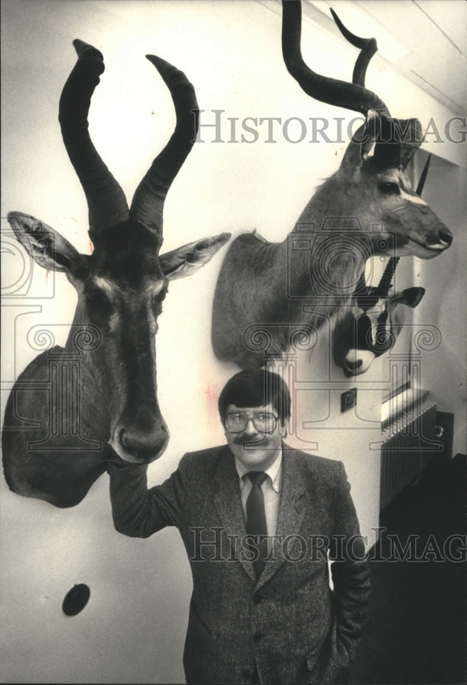 1988 Press Photo Frank J. Liska Jr. poses with his three hanging African animals - Historic Images
