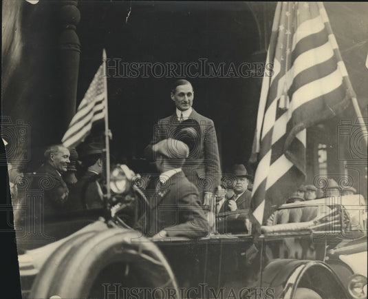 Press Photo Man in backseat of car between two American flags hand/hat on heart - Historic Images