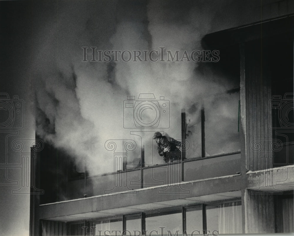 1986 Firefighter leans from a window during a fire, Milwaukee. - Historic Images