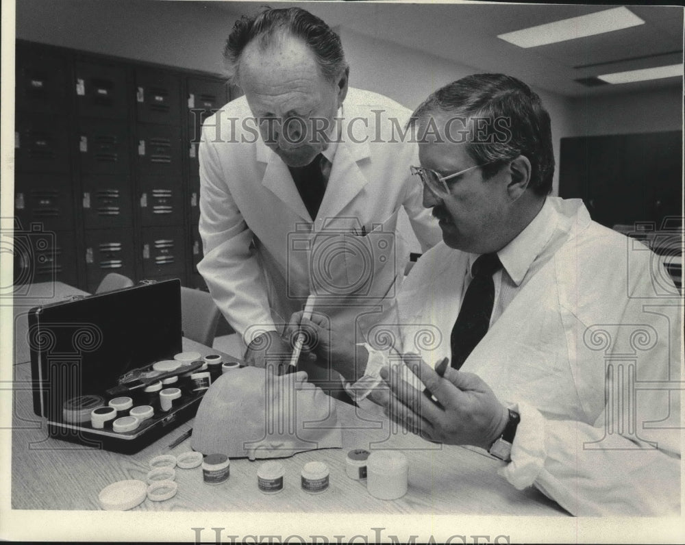 1986 Press Photo Ed Heidenreich watches student apply makeup to model face - Historic Images