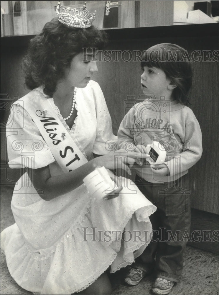 1982 Beauty Pagent contestant gives bank to child - Historic Images