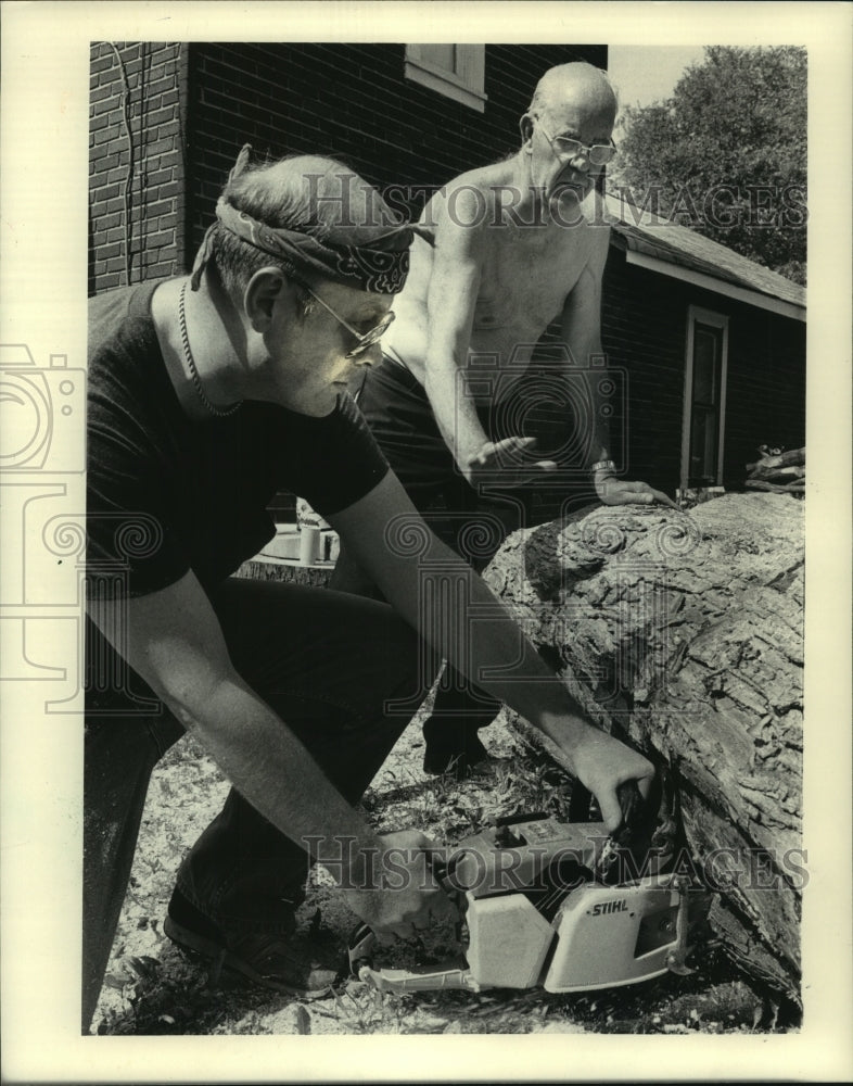 1983 Press Photo Men use chain saw to cut up a tree in Pewuakee Wisconsin - Historic Images