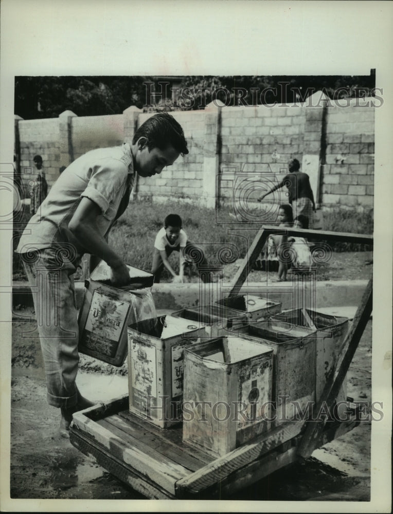 1962 Press Photo Young vender filling water cans to sell in Manila, Philippines- Historic Images
