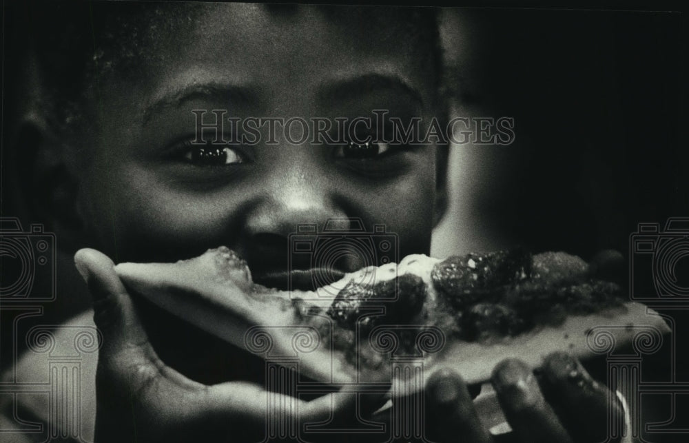1989 Girl bites into pizza at meal program, Saint Francis Seminary-Historic Images