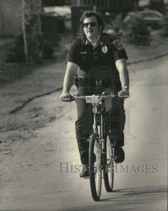 1986 Press Photo Schoonover, policeman riding bike in parking lot, Wisconsin. - Historic Images