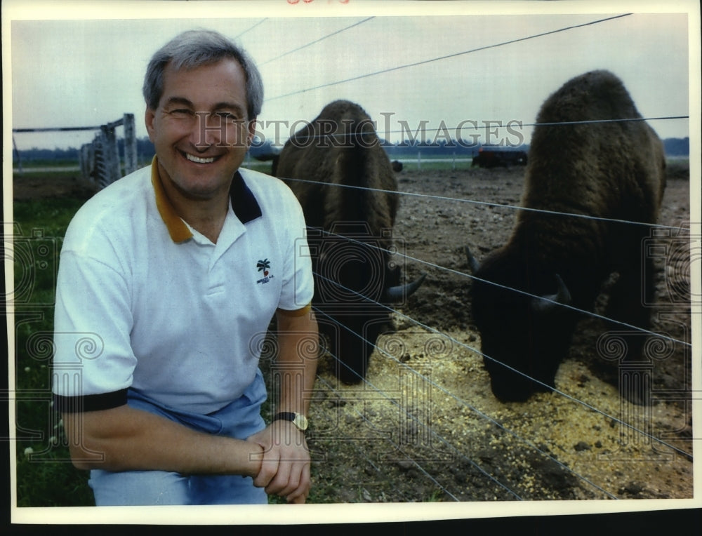 1993 Press Photo Ralph Stayer sits in front of two buffalo eating - mjb92208 - Historic Images