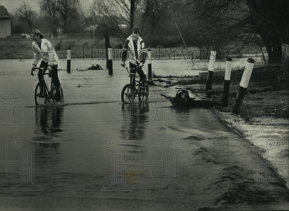 1989 Press Photo Kevin Peters, Mike Adams ride bikes through water, Saukville - Historic Images