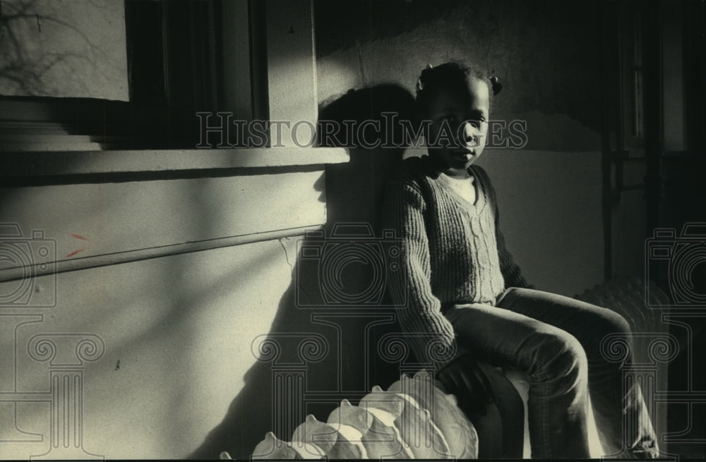 1986 Press Photo Young resident girl sits on radiator at shelter - mjb94801 - Historic Images