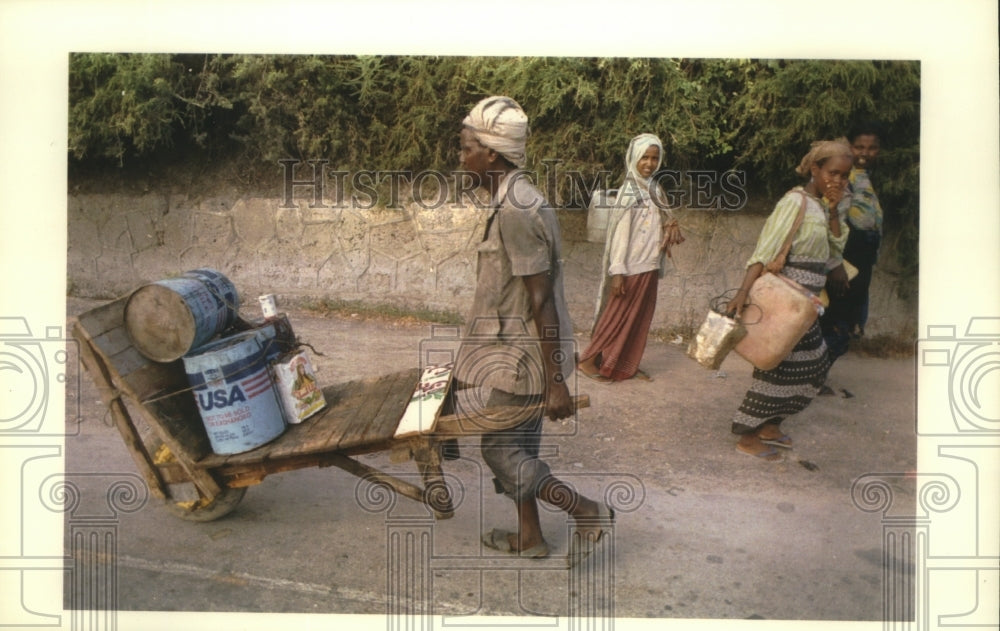 1992 Somali man pushes cart of looted American relief supplies. - Historic Images