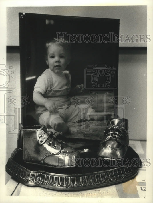 1993 A bronzed pair of baby shoes with a photograph of its owner - Historic Images