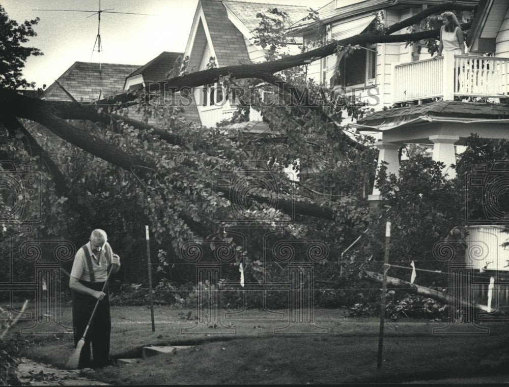 1989 Press Photo Man in Shorewood sweeps debris from sidewalk after storm - Historic Images