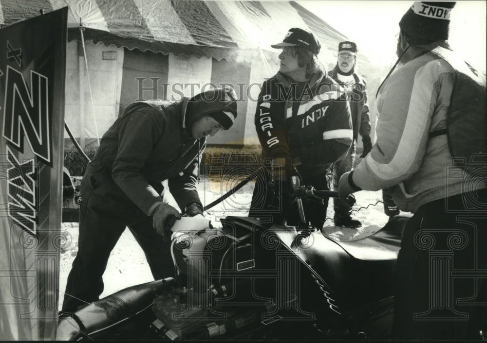 1994 Pit crew member Doug Schwauns puts oil into snowmobile engine. - Historic Images
