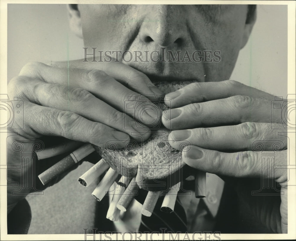1984 Man eats cigarette sandwich in anti-smoking campaign. - Historic Images