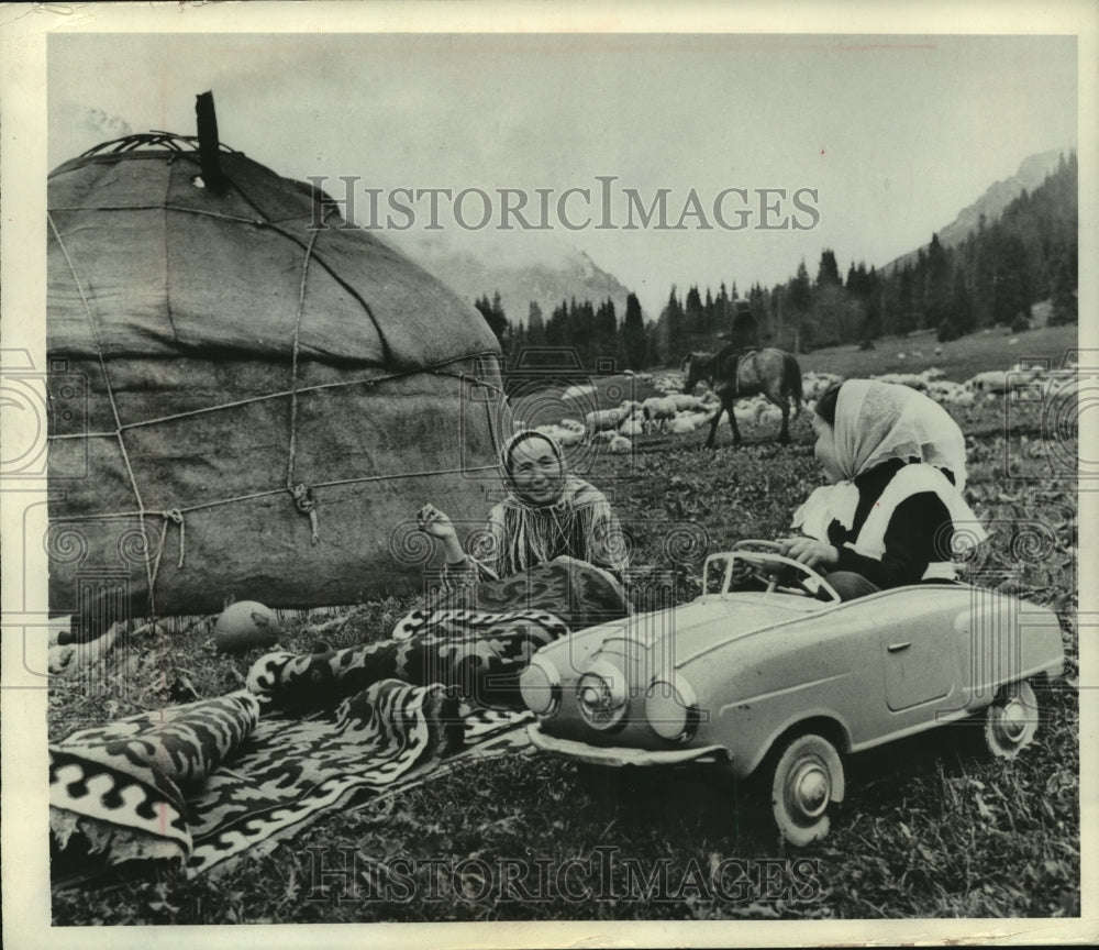 1966 Press Photo Child plays in toy car while her mother sews in Kirghiza Russia - Historic Images