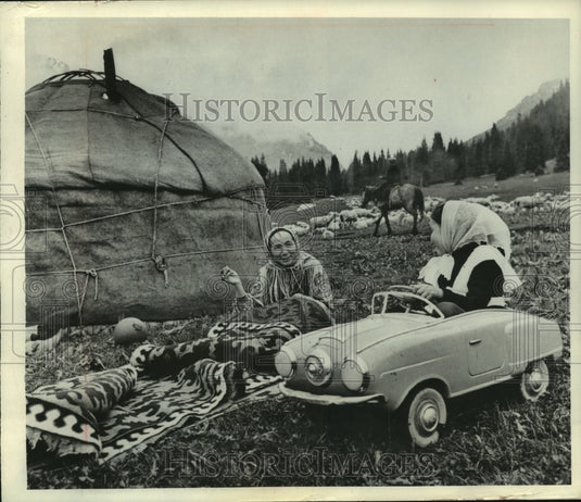1966 Press Photo Child plays in toy car while her mother sews in Kirghiza Russia - Historic Images
