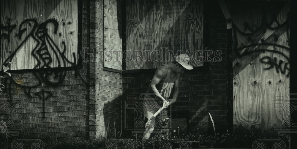 1990, Fidel Martinez cuts down weeds as part of alley clean up - Historic Images