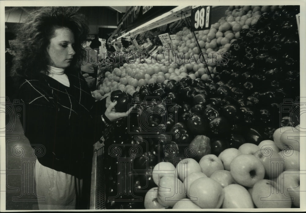 1989 Press Photo Teenager Sara Counter examines apples while grocery shopping - Historic Images