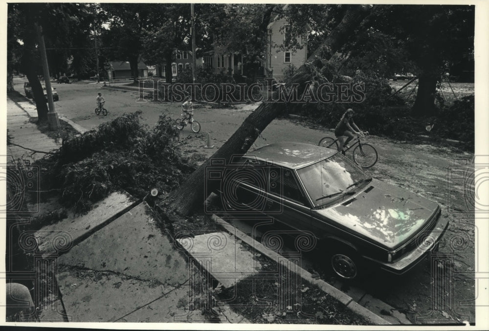 1991 Press Photo Cyclists ride past a crushed car on Hilbert Ave. in Cedarburg - Historic Images