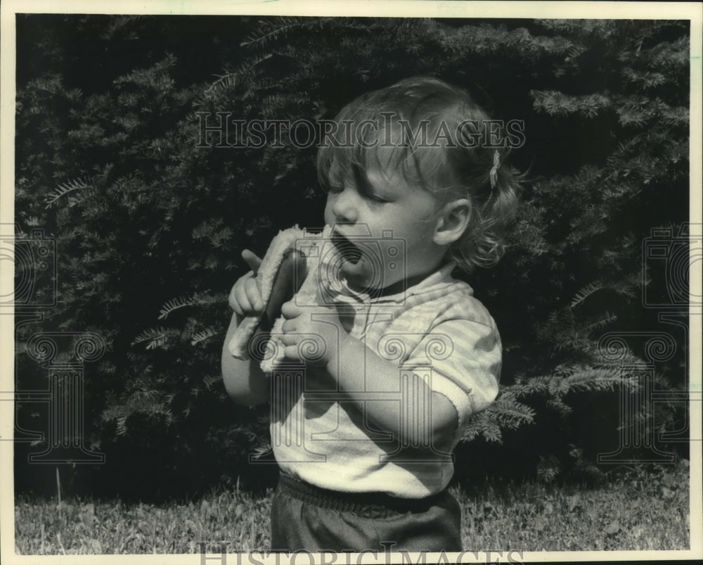1983, Sara Miller eats a hot dog at a picnic near South Range - Historic Images